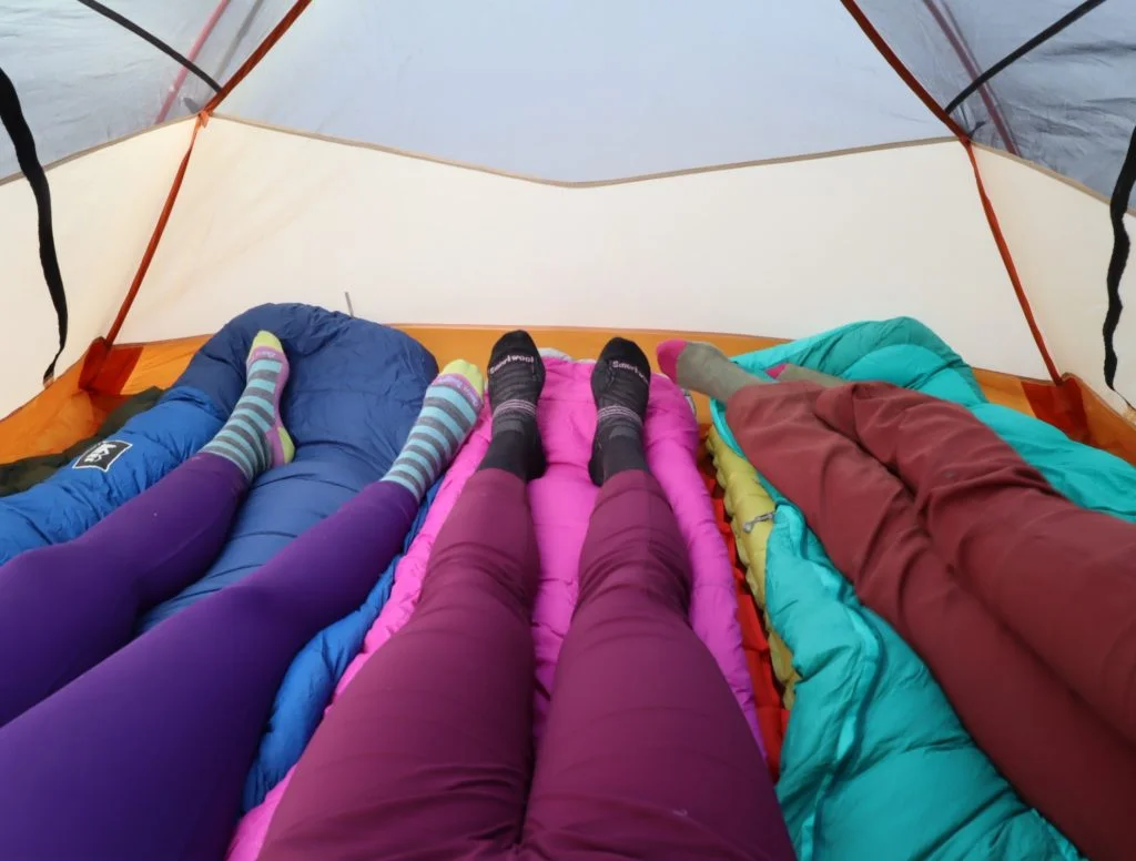 three women in a tent with colorful sleeping bags | how to wash your down sleeping bag