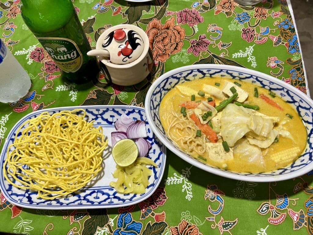 Two bowls of noodles from thailand on a budget and a bottle of beer on a table.